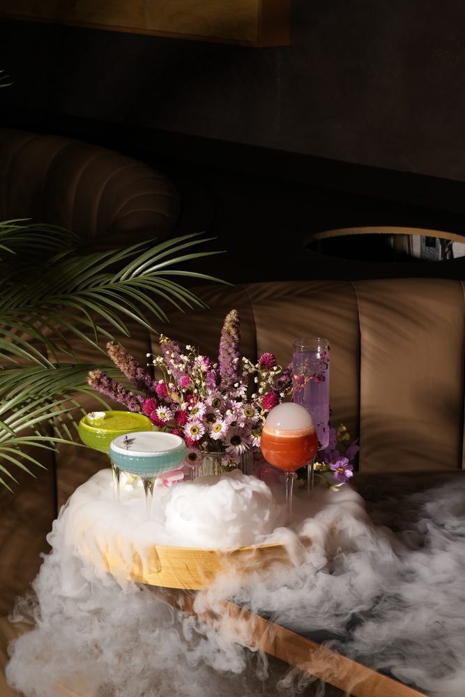 A trio of colourful summer cocktails on a smoky table with dried flowers